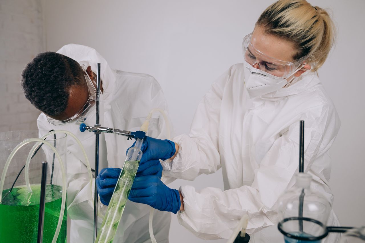 Researchers in protective gear conducting a controlled lab experiment with green liquid.